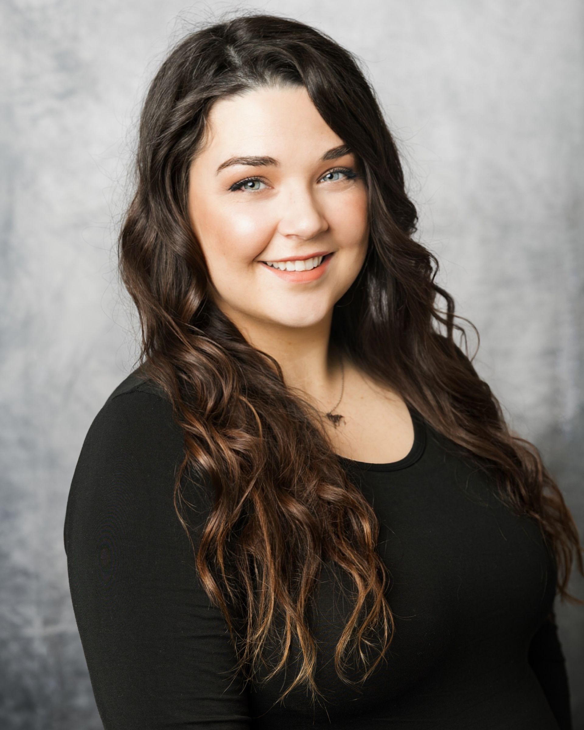 A woman with red hair and glasses is wearing a blue shirt and smiling.
