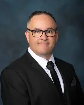A man in a suit and tie is standing in front of a blue background.