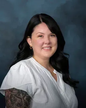 The woman is wearing a white shirt and has a tattoo on her arm.
