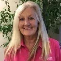 A woman with long blonde hair is wearing a pink shirt and smiling.