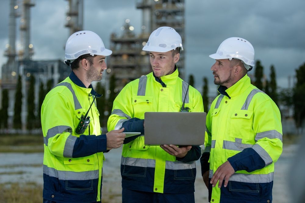 A group of construction workers are standing next to each other looking at a laptop.