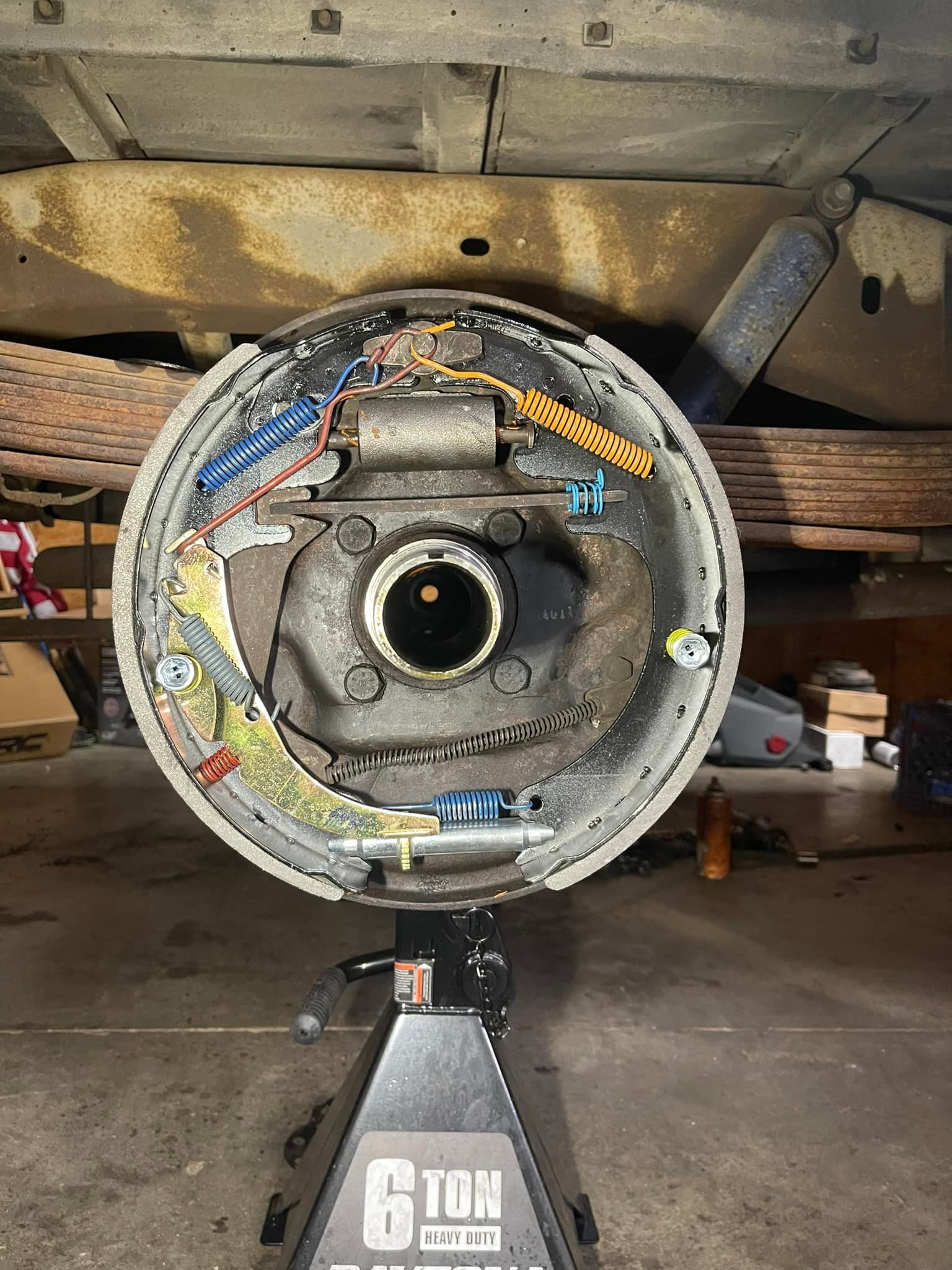 Rear drum brake assembly, detached from vehicle, supported by jack stand. Wiring and brake components visible.