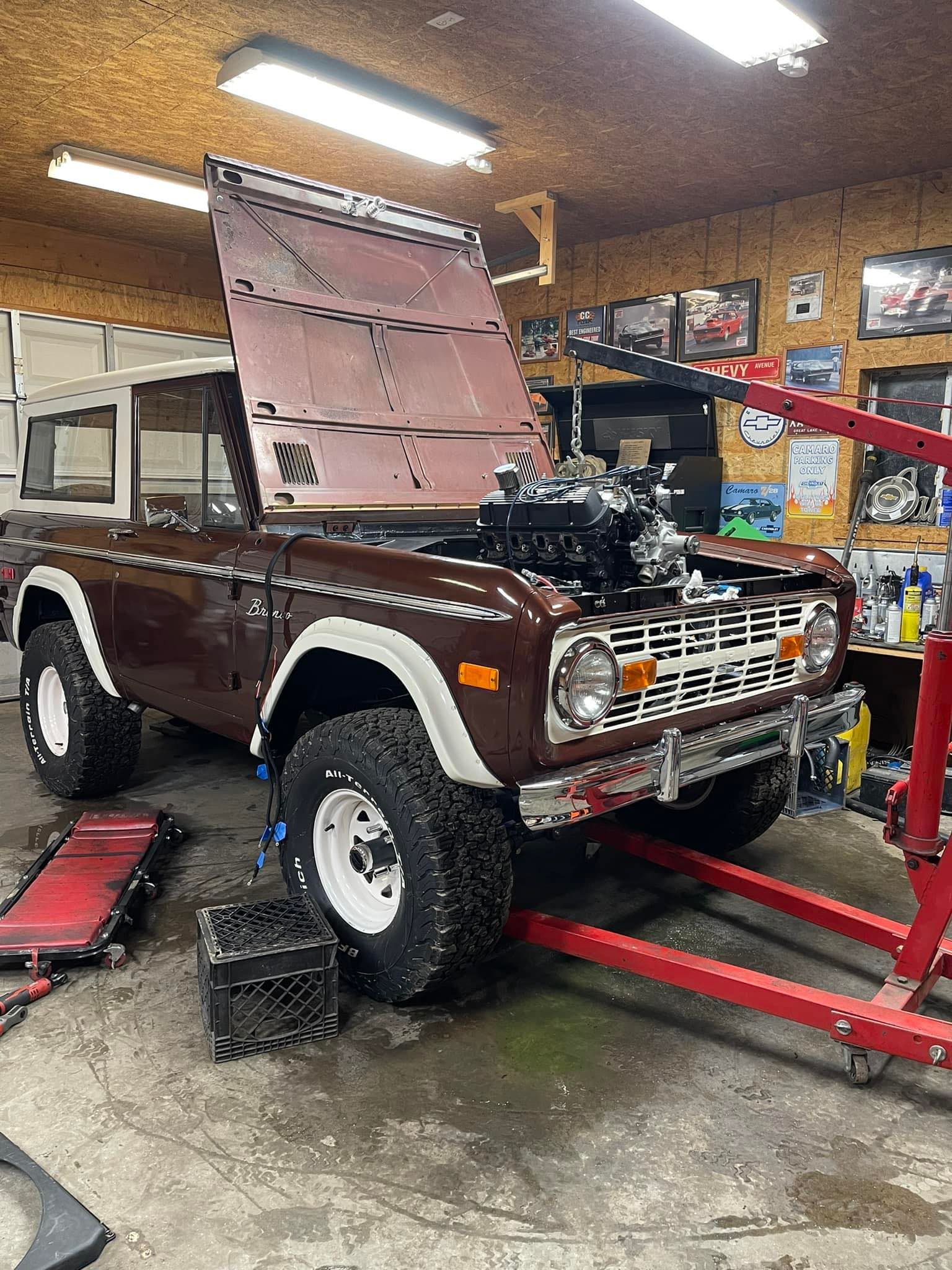 Brown Ford Bronco with hood up, engine being worked on, in a garage.