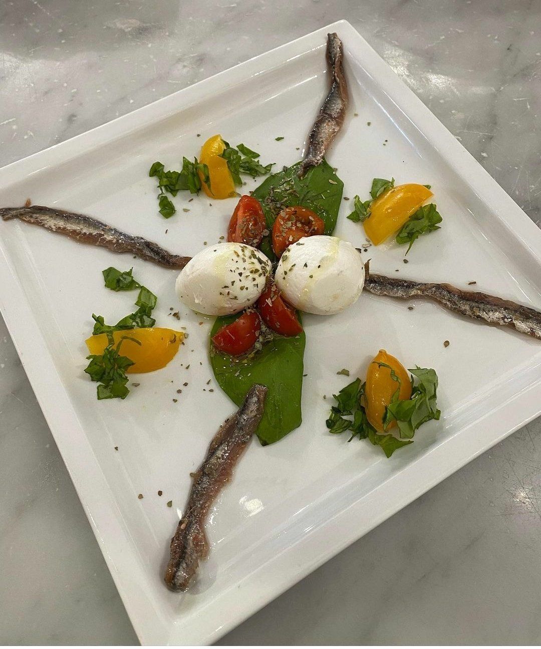 Un piatto bianco condito con acciughe, pomodori e mozzarella