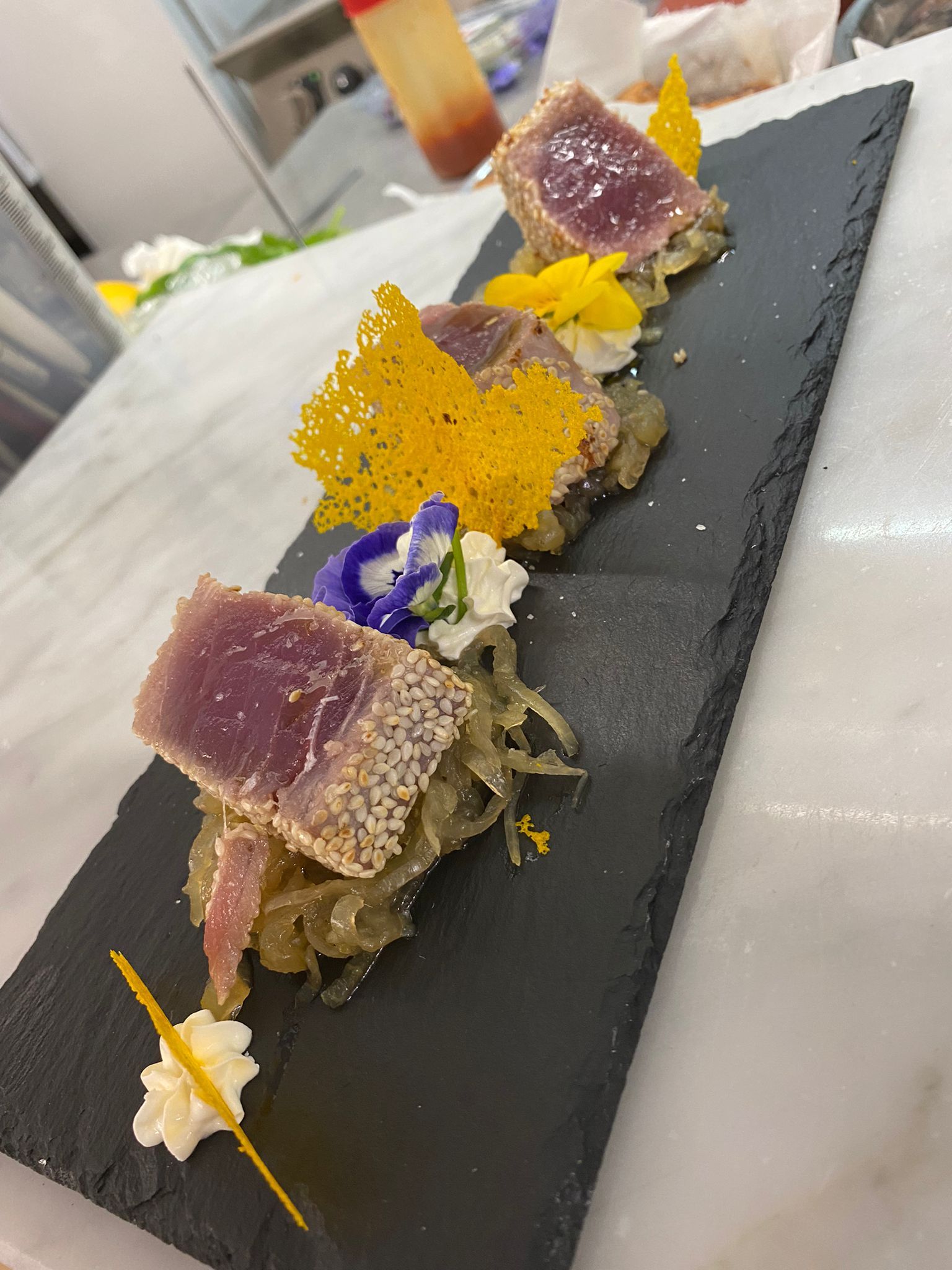 Un vassoio di ardesia nera pieno di cibo e fiori su un tavolo.