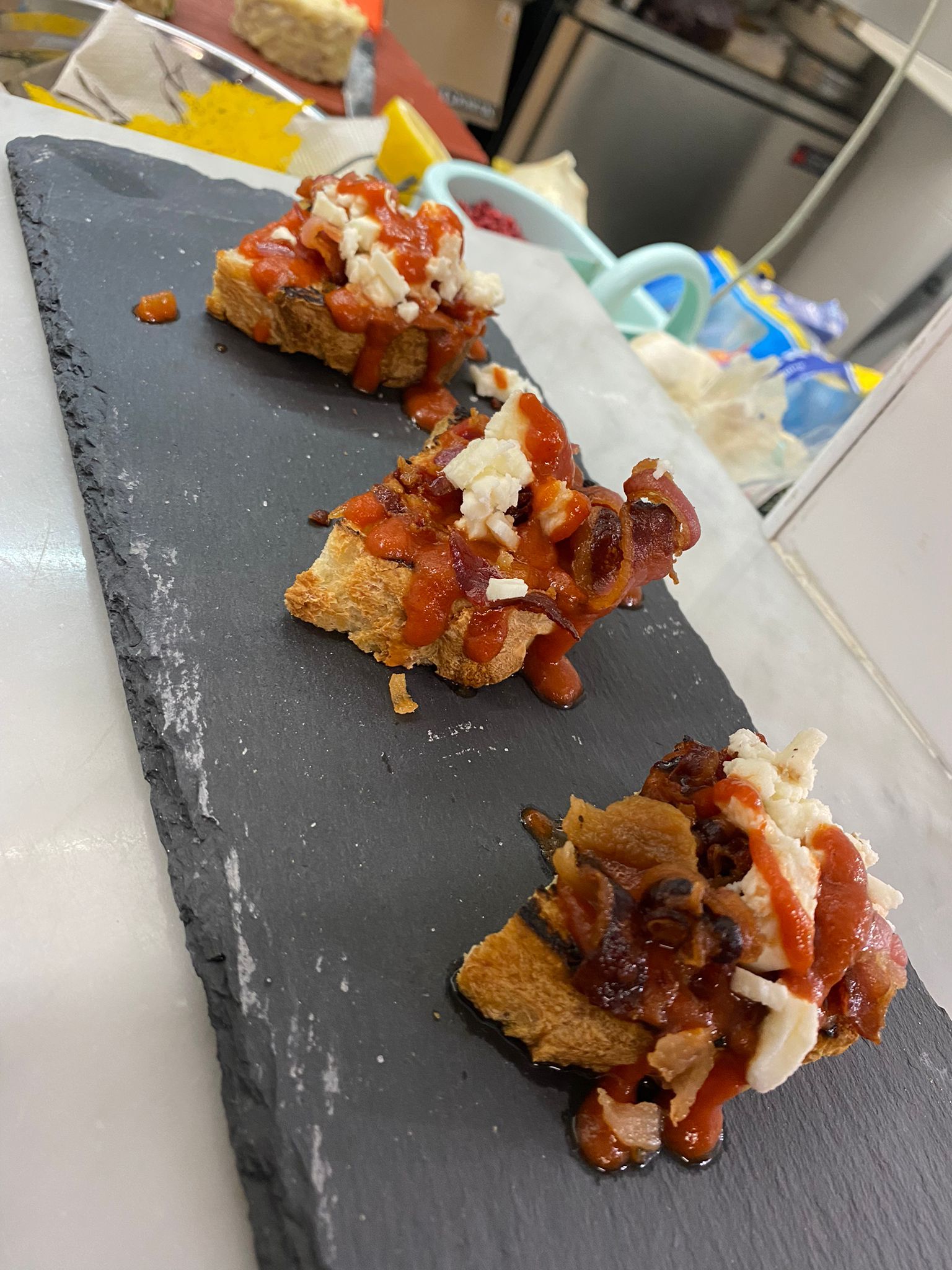 Tre pezzi di cibo sono su un vassoio di ardesia su un tavolo.