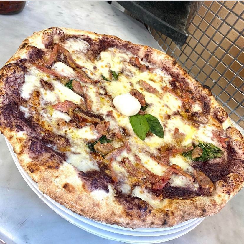 Una pizza è appoggiata su un piatto bianco su un tavolo.