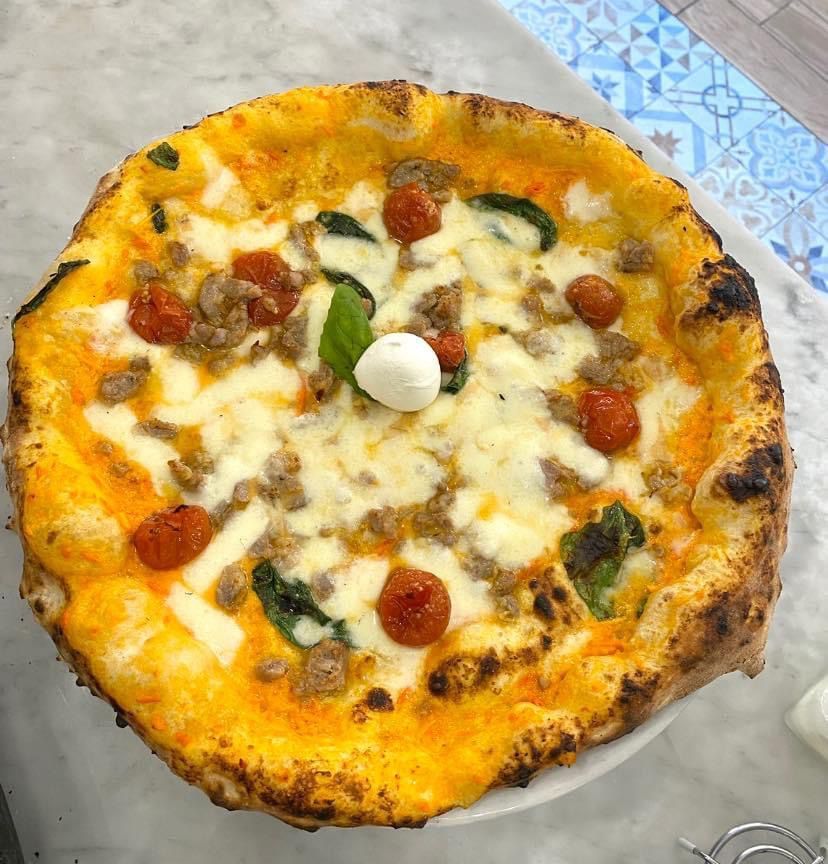 Una pizza con pomodori, salsiccia, formaggio e basilico su un piatto su un tavolo.