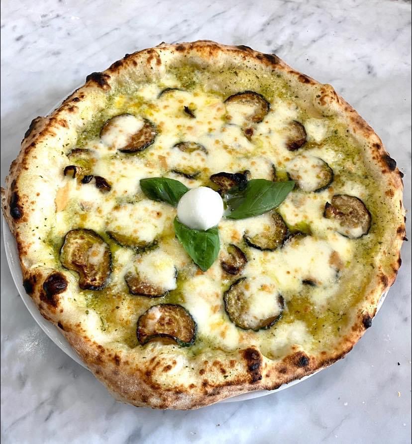 Una pizza con melanzane e formaggio su un piatto bianco