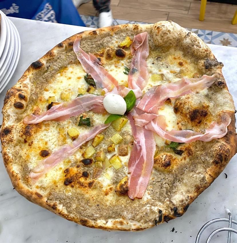 Una pizza con pancetta e formaggio è su un tavolo.
