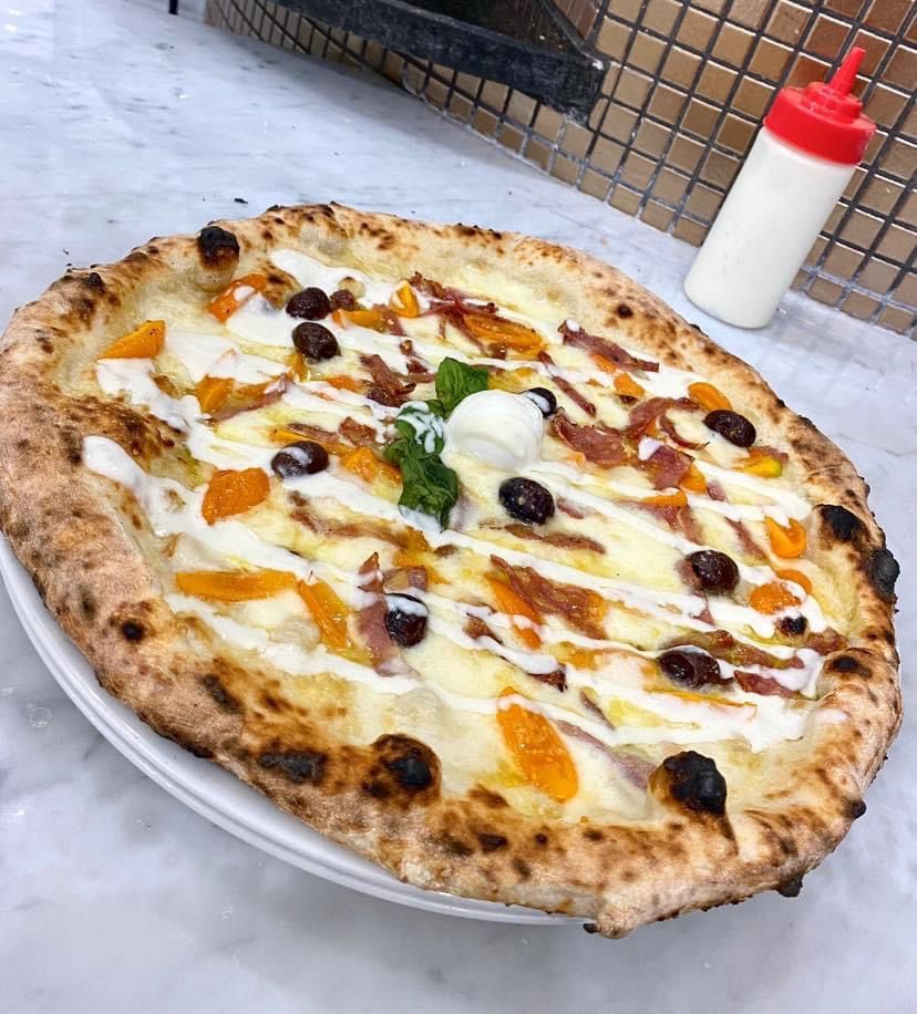 Una pizza è appoggiata su un piatto bianco accanto a una bottiglia di salsa.