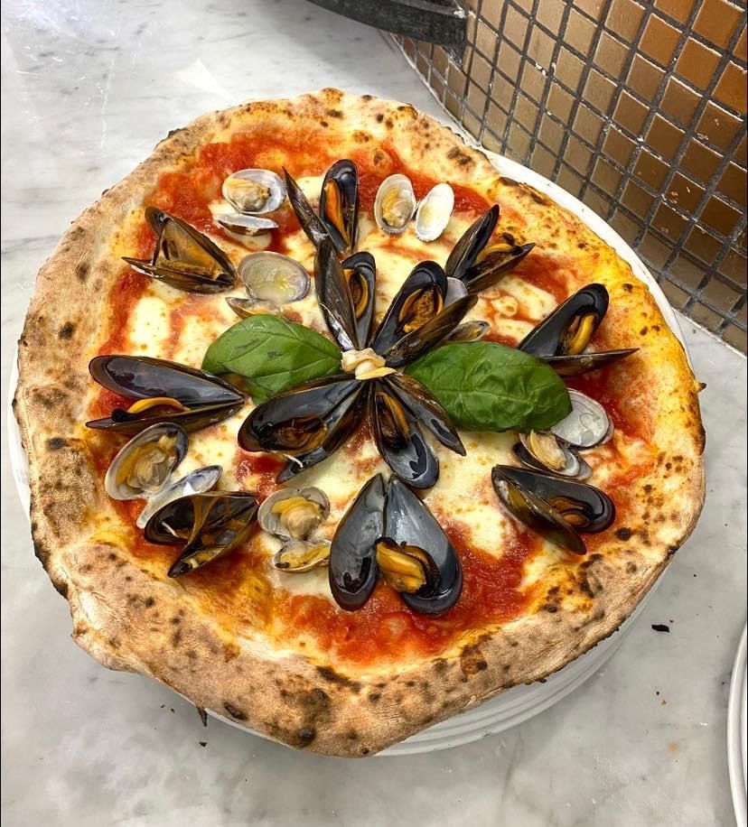 Una pizza con cozze e basilico sopra