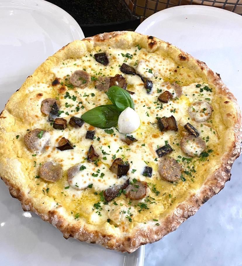 Una pizza con funghi e melanzane servita su un piatto bianco.