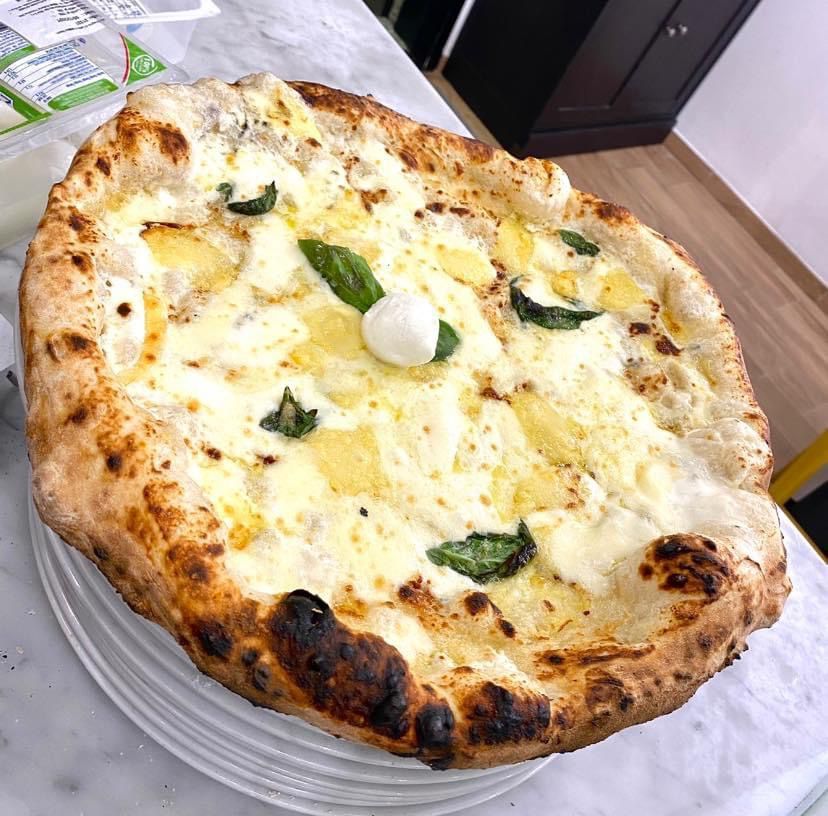 Una pizza con tanta mozzarella appoggiata su una pila di piatti su un tavolo.