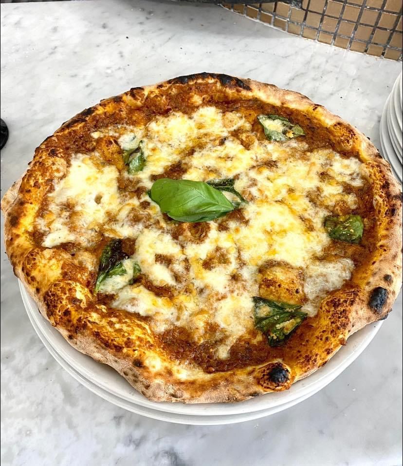 Una pizza margherita appoggiata su un piatto bianco su un tavolo.