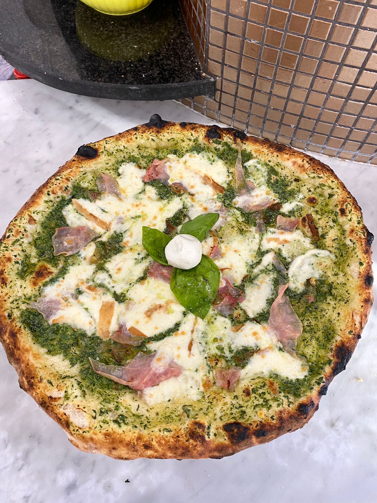 Una pizza con pesto e basilico appoggiata su un tavolo.