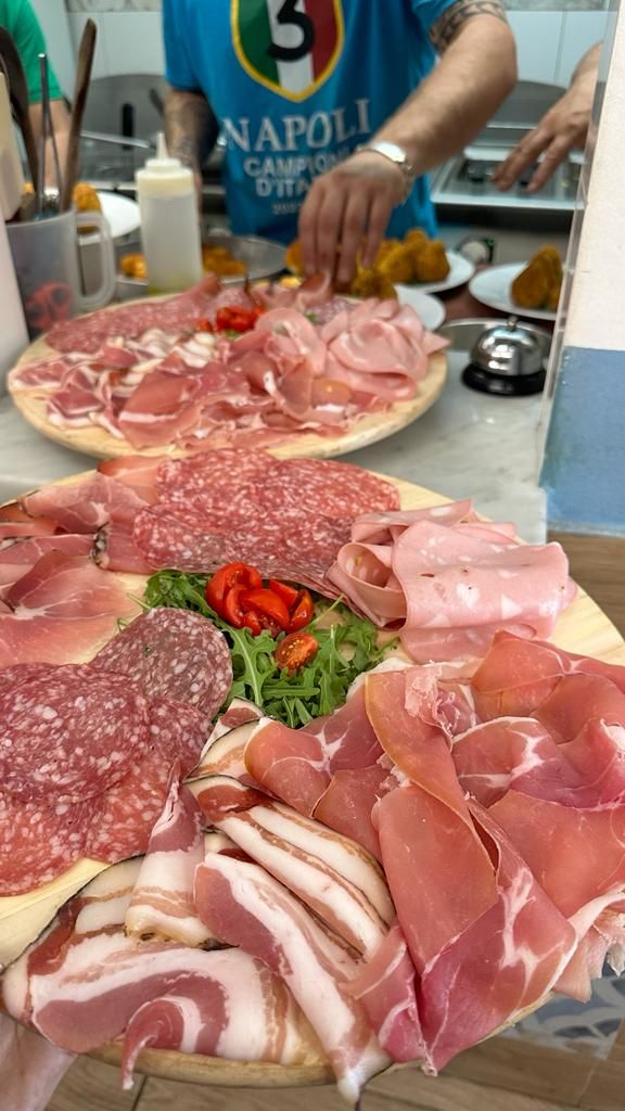 Una persona tiene in mano un piatto di carne accanto a una pizza.