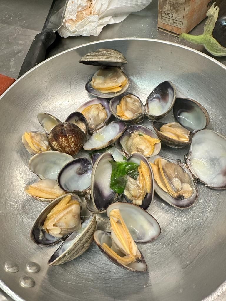 Una padella piena di vongole è appoggiata sul bancone.