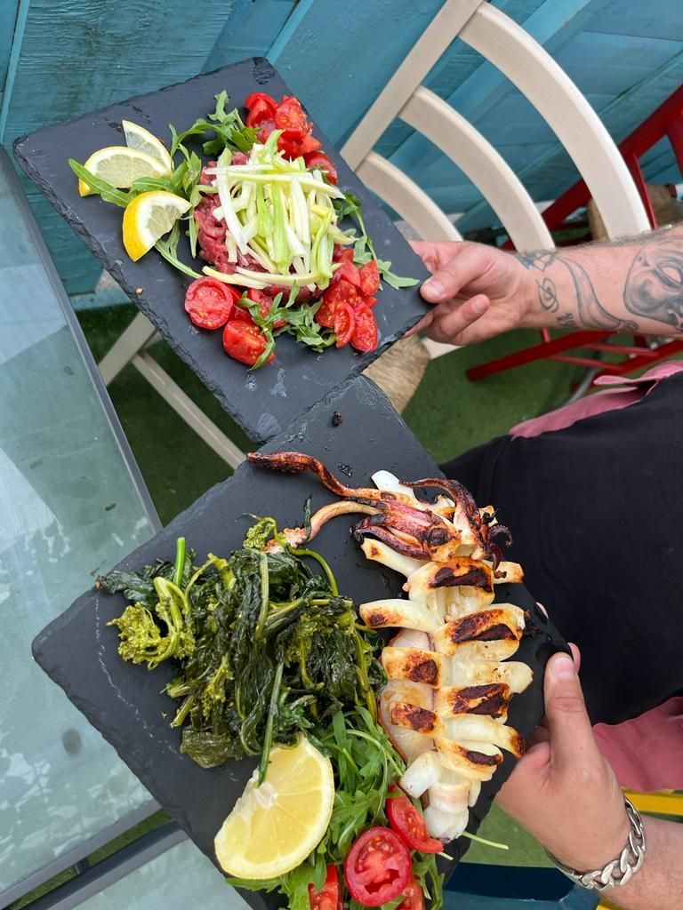 Una persona tiene in mano due piatti di cibo su un tavolo.