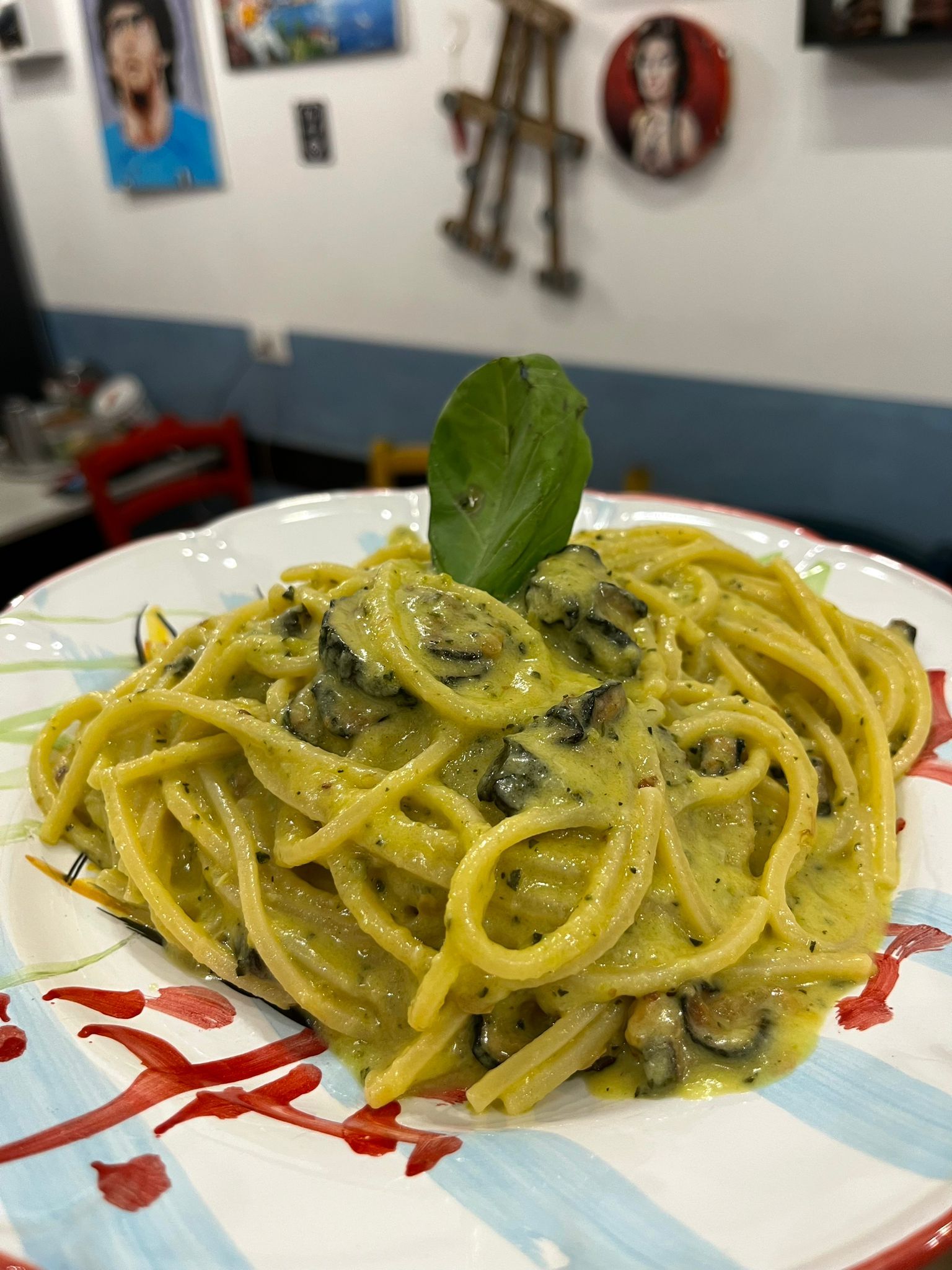 Un piatto di spaghetti con salsa verde e una foglia di basilico sopra.