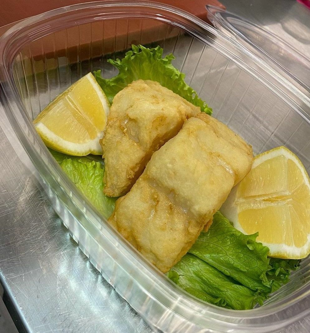 Un contenitore di plastica pieno di pesce fritto, lattuga e fette di limone.