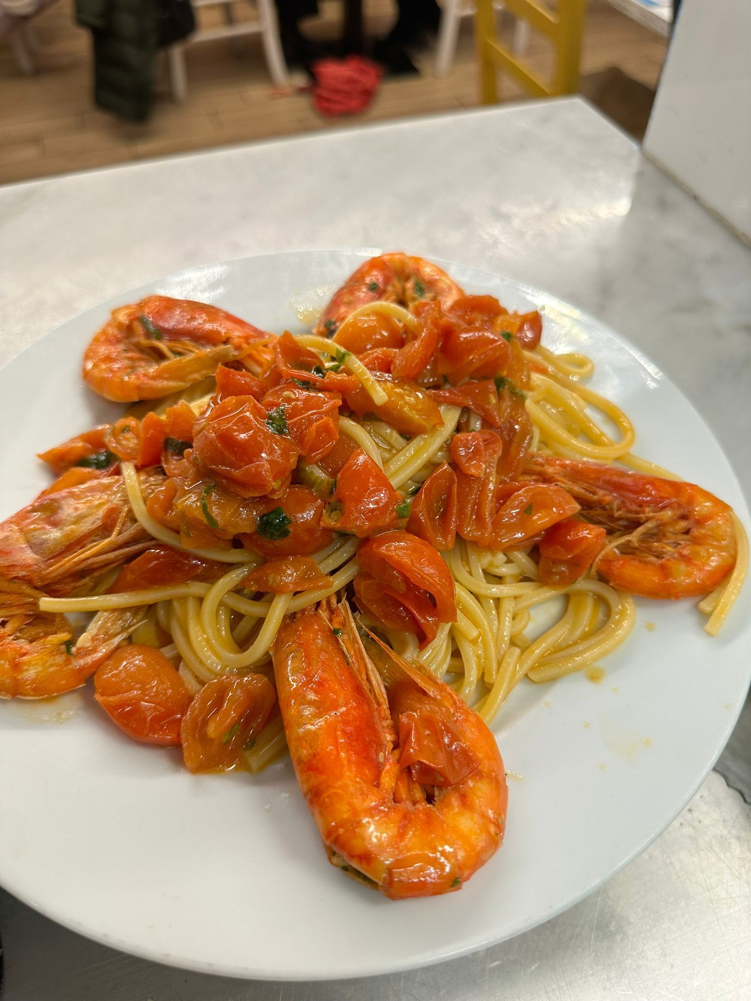 Un piatto bianco con sopra spaghetti e gamberi su un tavolo.