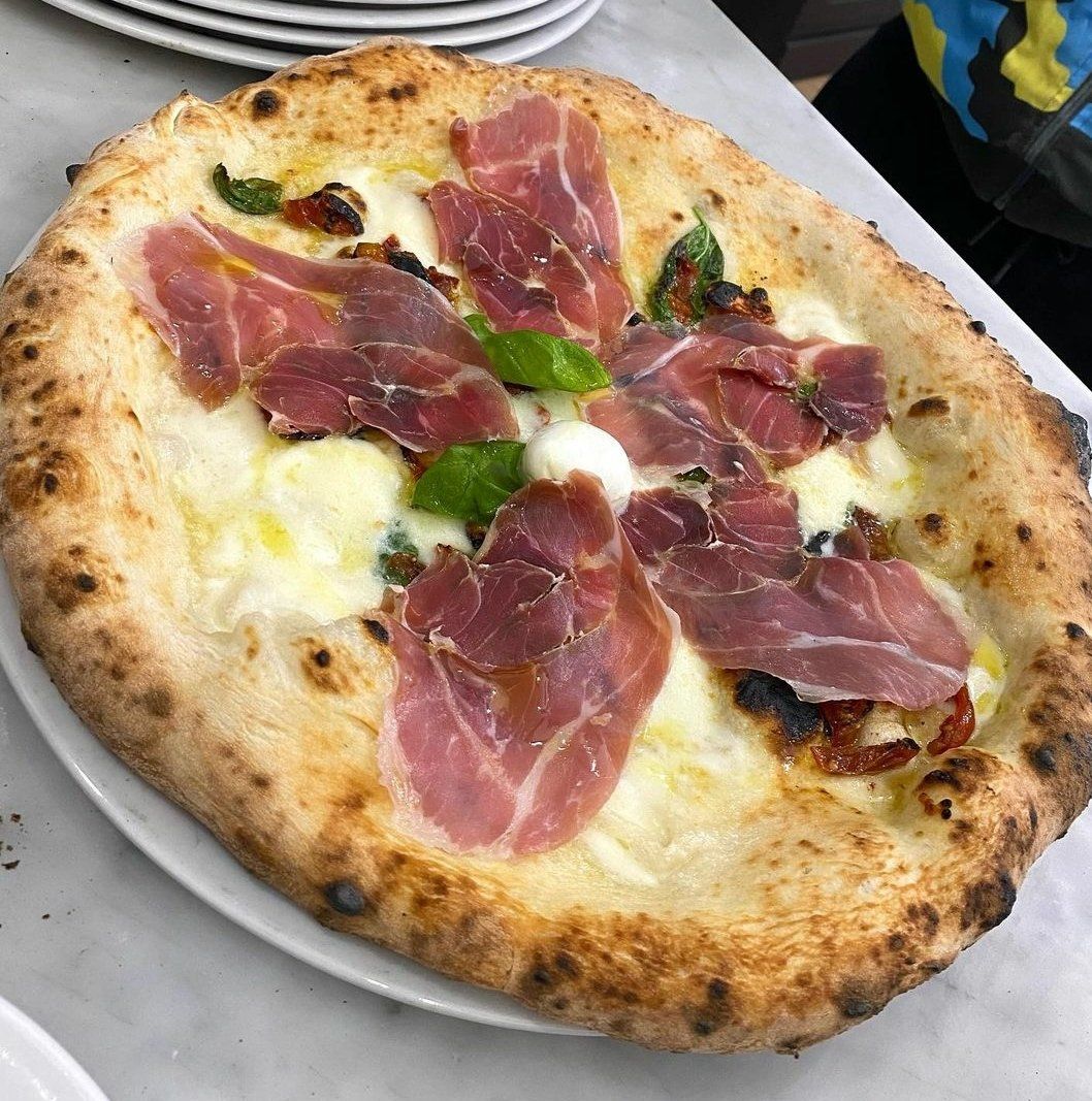 Una pizza con prosciutto e formaggio su un piatto bianco su un tavolo.