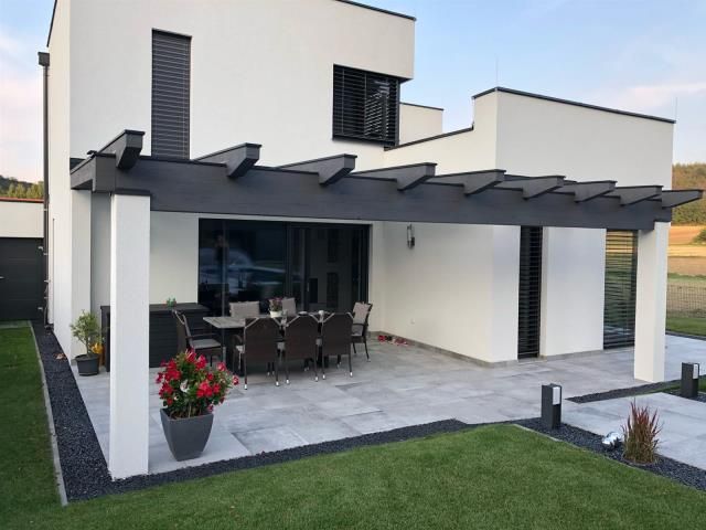Ein weißes Haus mit einer Terrasse mit Tisch und Stühlen unter einer Pergola.
