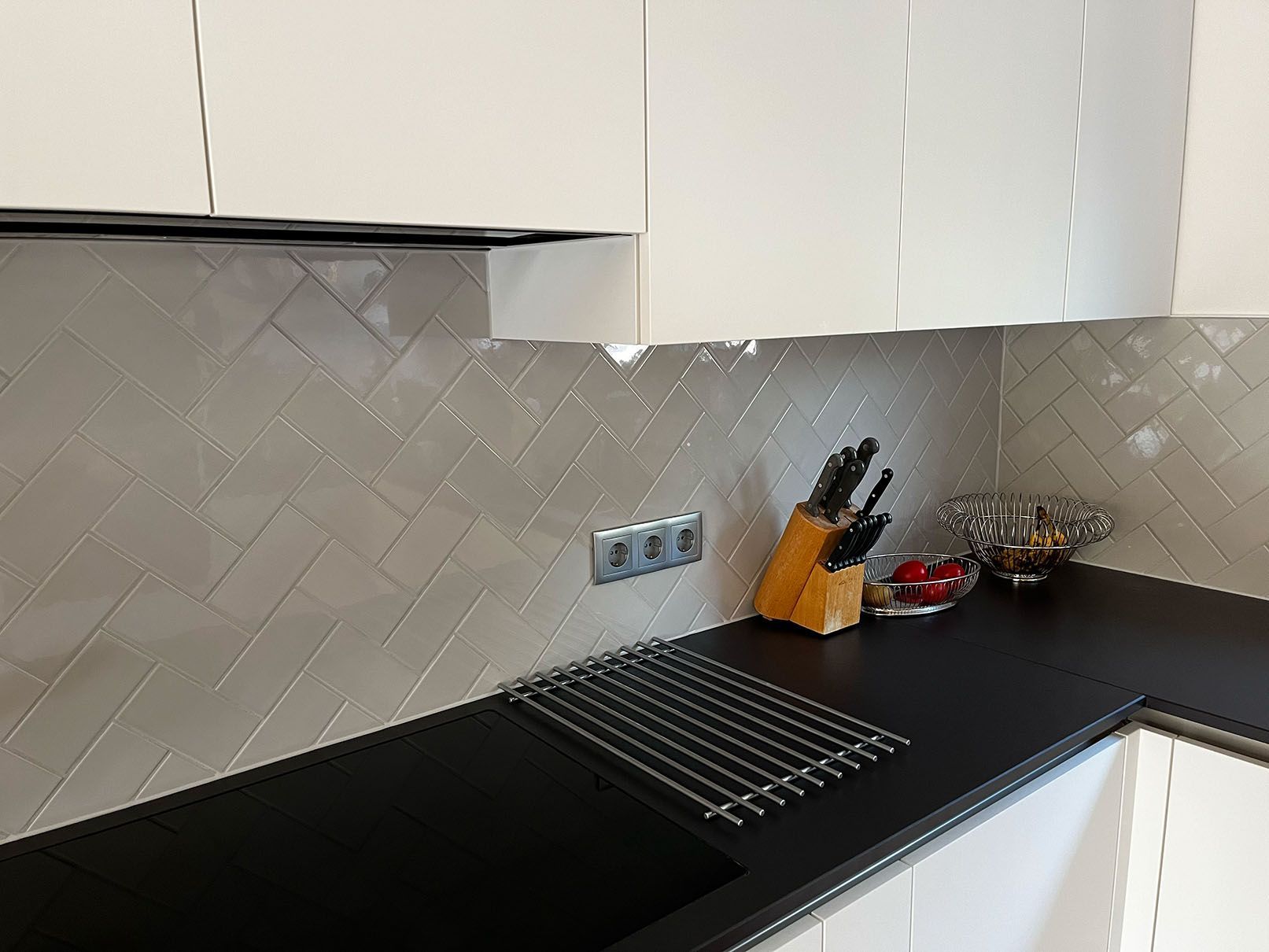 Eine Küche mit weißen Schränken, grauen Wandfliesen im Fischgrätenstil und einer schwarzen Arbeitsplatte.
