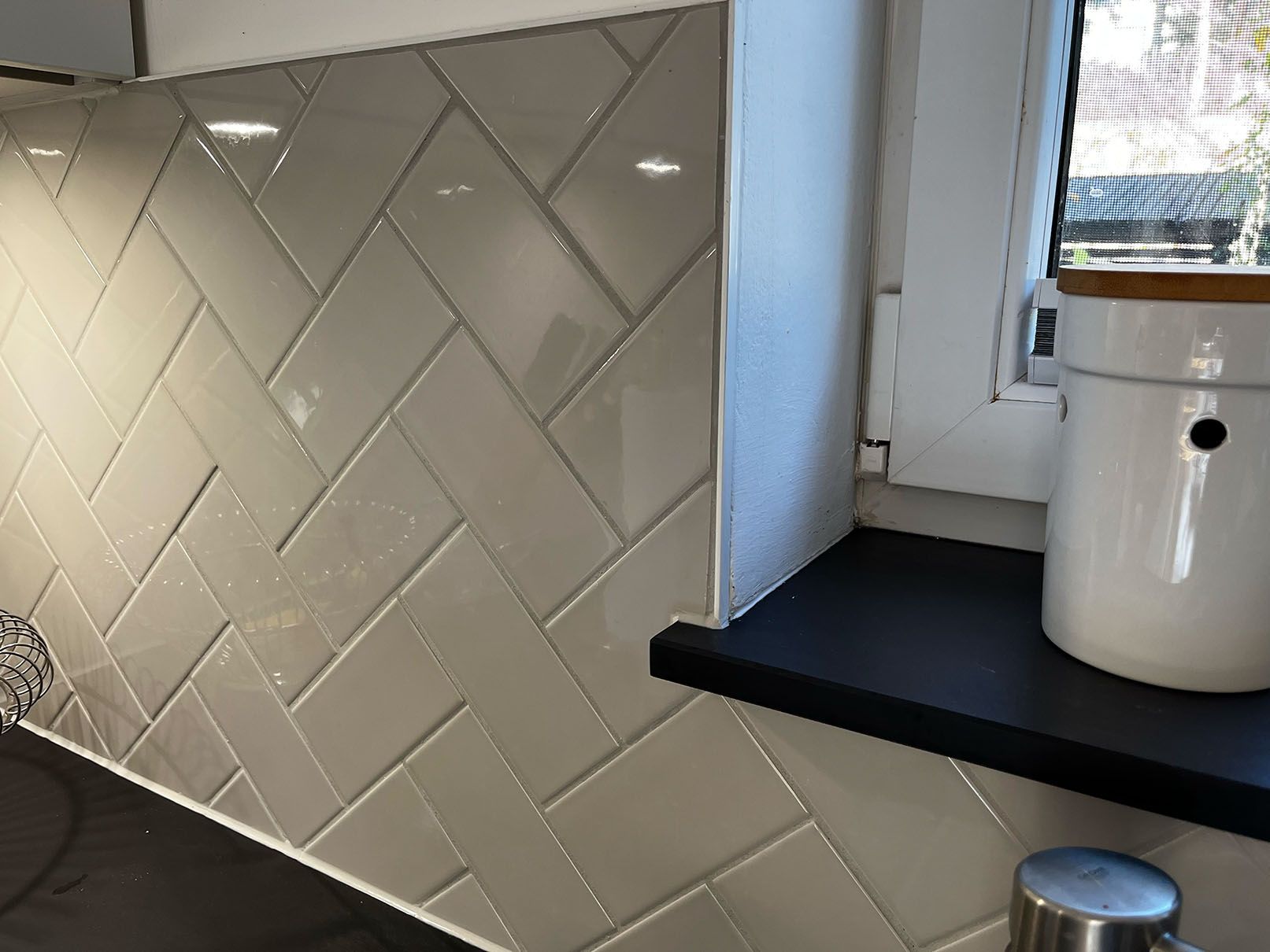 Eine Küchentheke mit grauen Fliesen und einem Fenster.