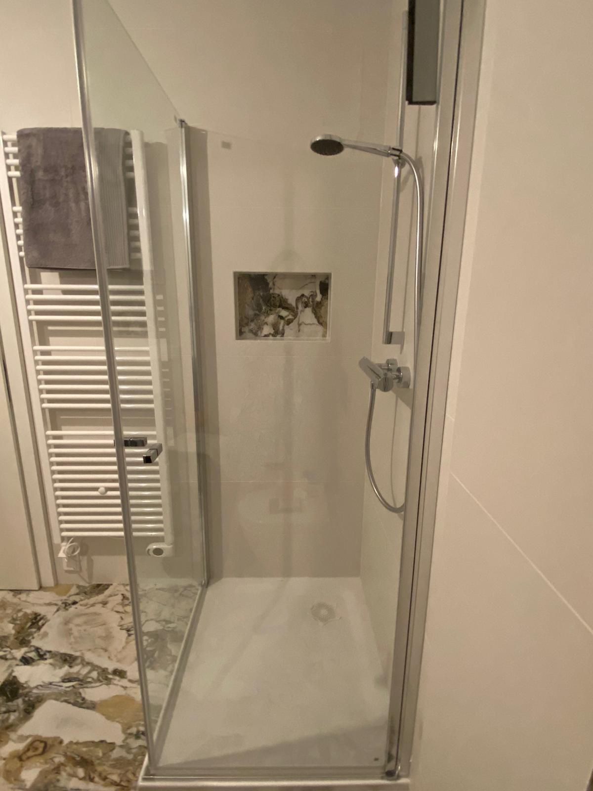 Ein Badezimmer mit großen Fliesen, ebenerdiger Dusche und Handtuchhalter.