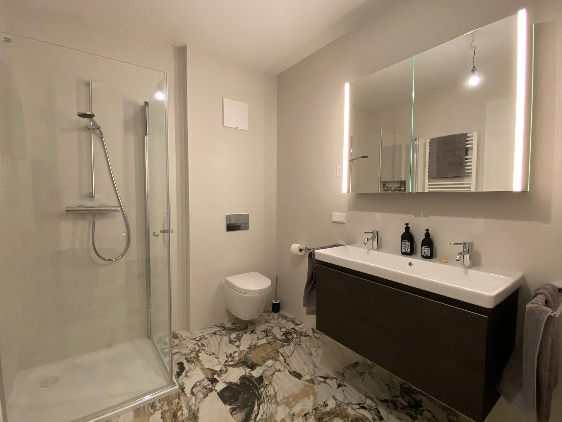 Ein Badezimmer mit Marmorfliesen, Toilette, Waschbecken, Dusche und Spiegel.