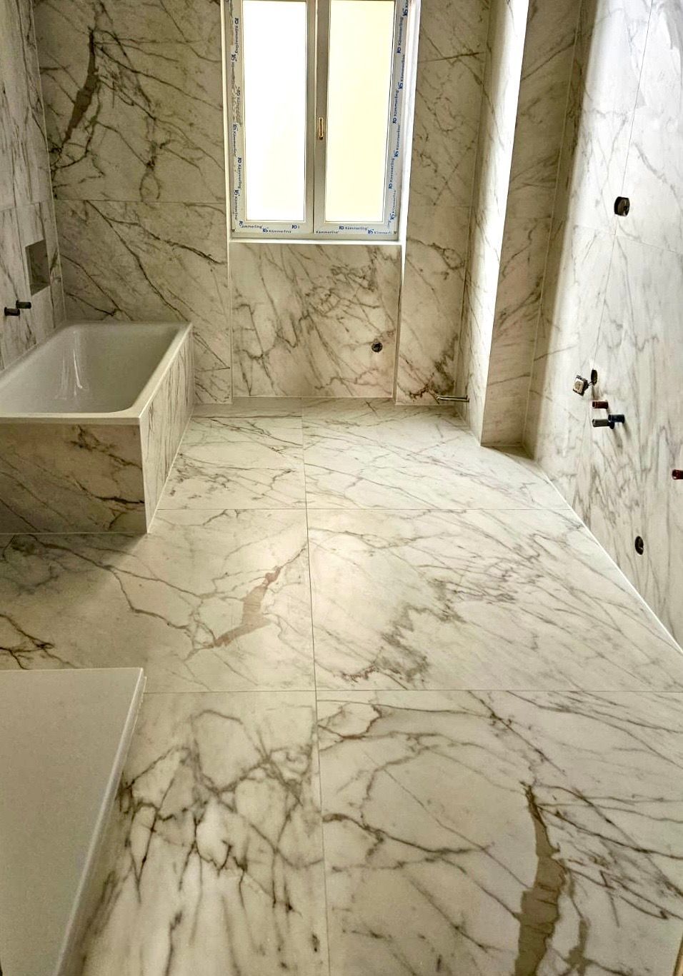 Ein Badezimmer mit Marmorfliesenwänden und -böden und einer Badewanne.