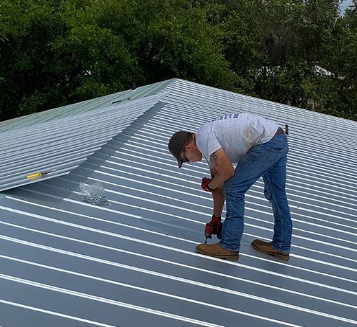 A man is working on a metal roof with a drill.