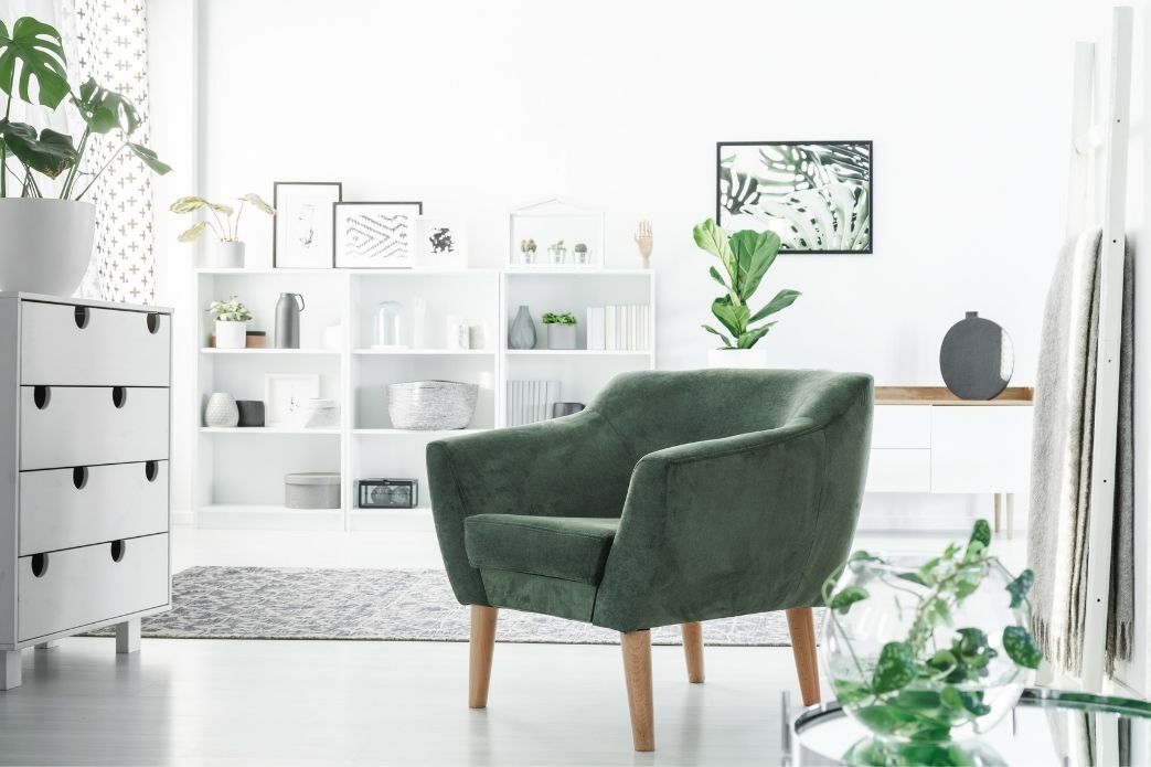 A green chair is sitting in a living room next to a bookshelf.