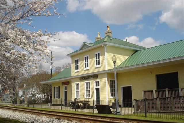 A yellow building with a green roof is next to train tracks.