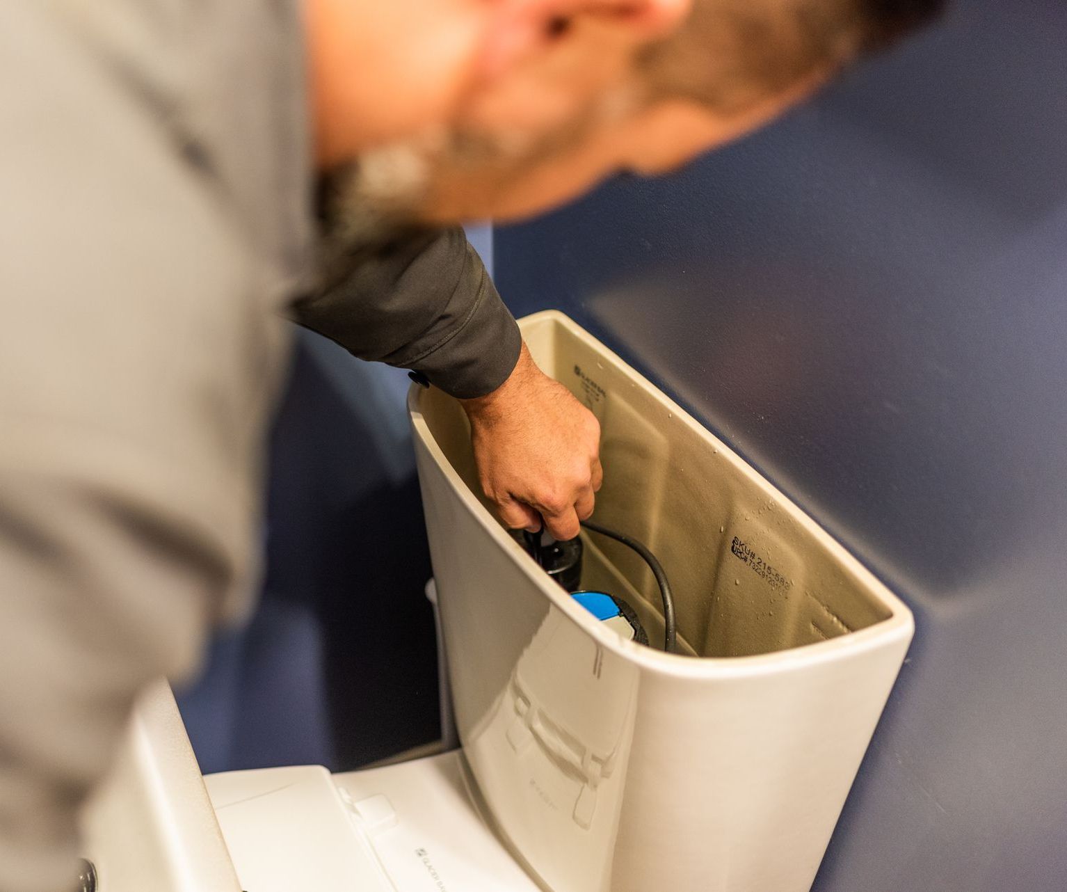 A man is fixing a toilet with a screwdriver