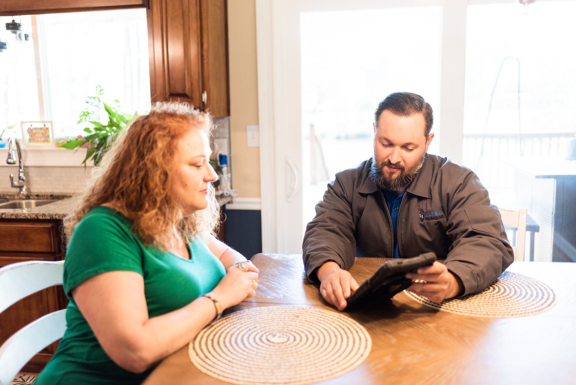 A man and a woman are sitting at a table looking at a tablet.