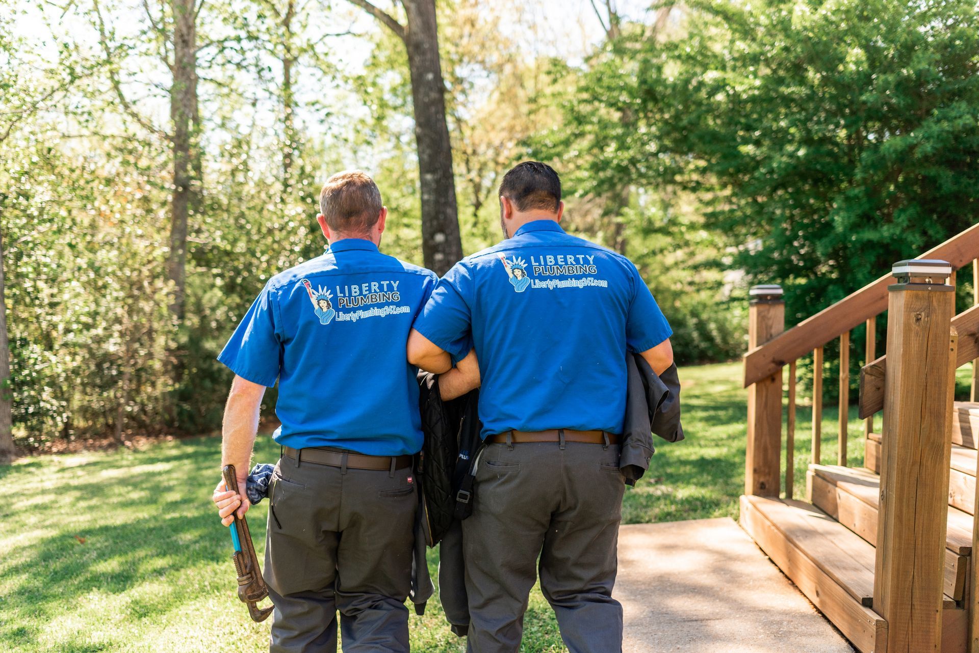 Two men in blue shirts are walking down a sidewalk.