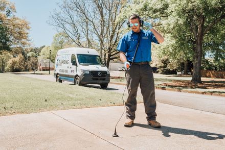 A man wearing headphones is standing on a sidewalk next to a van.