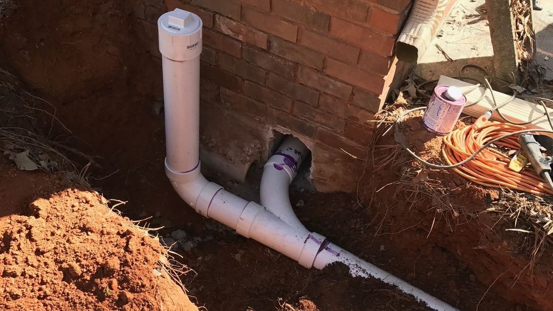 A white pipe is laying in the dirt next to a rock.