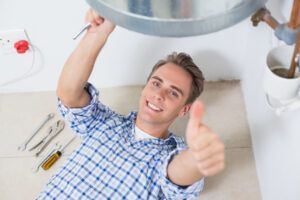 A man is giving a thumbs up while fixing a pipe.