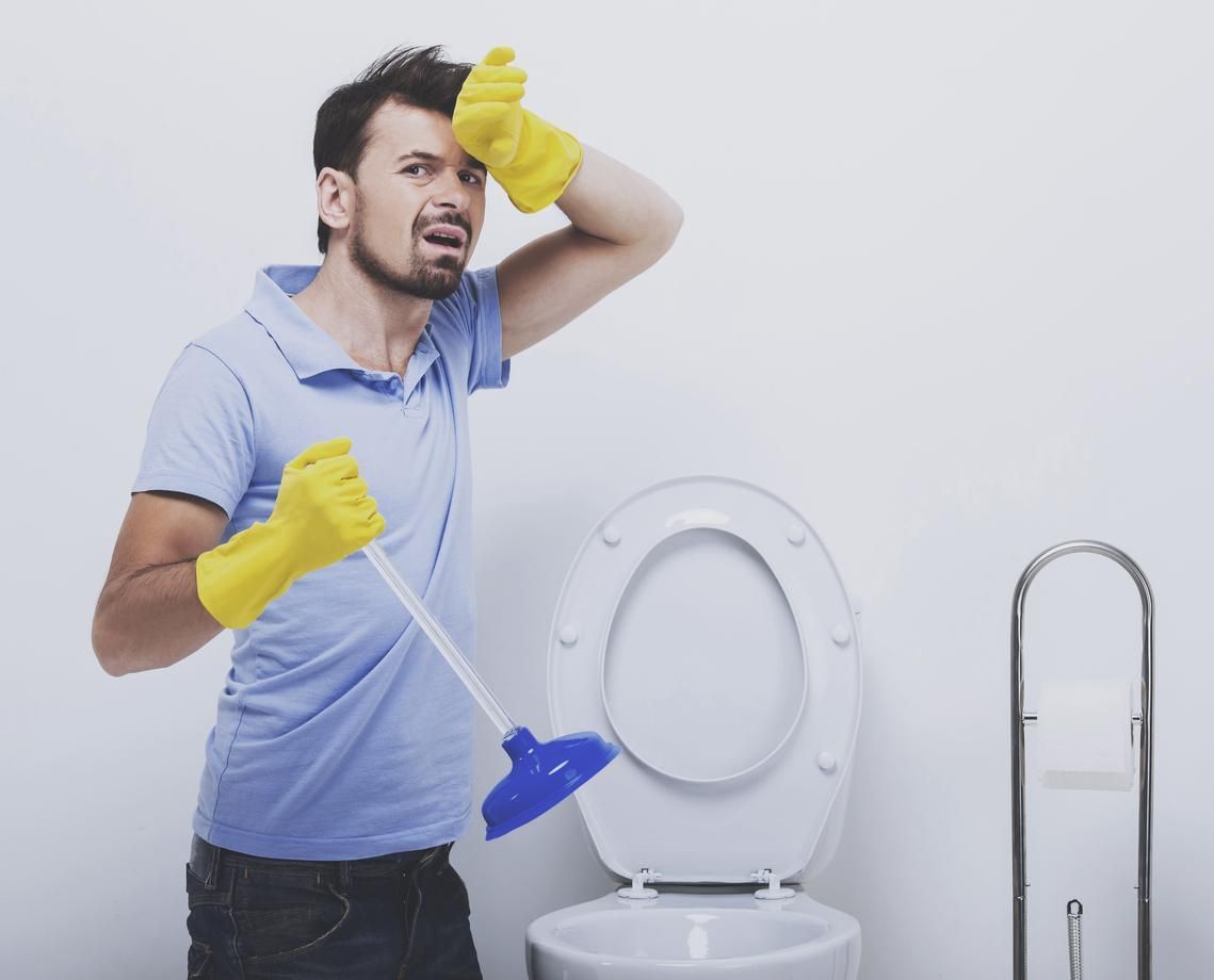 A man is holding a plunger in front of a toilet.