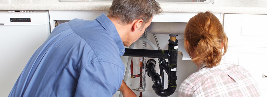 A man and a woman are fixing a sink in a kitchen.