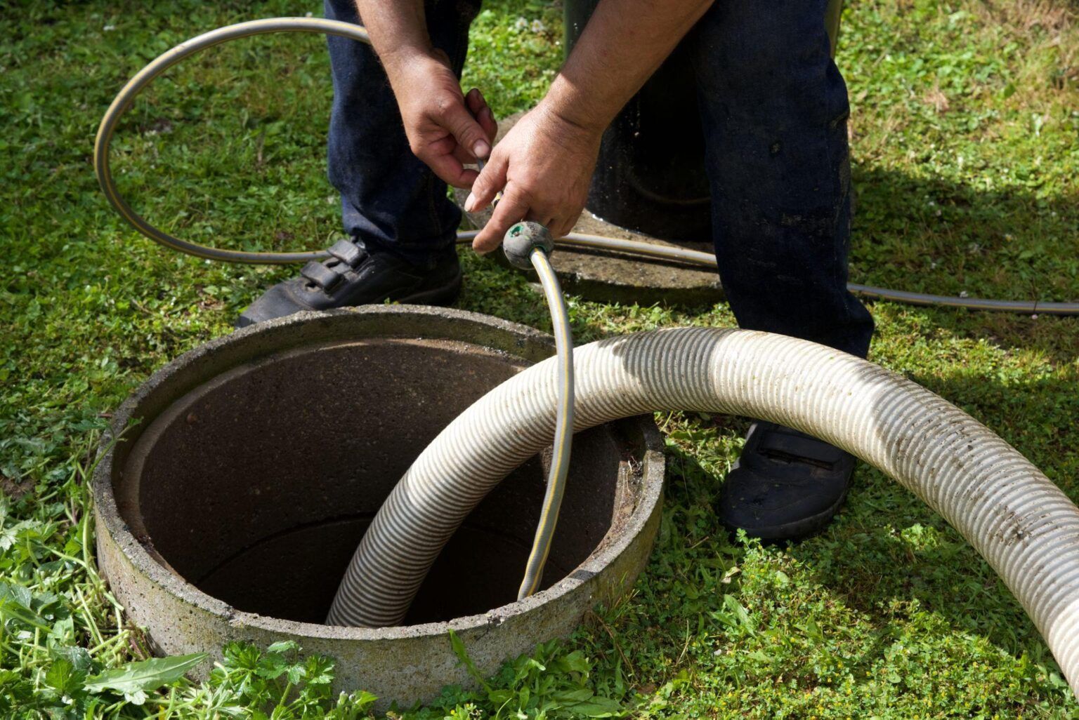 A man is pumping a hose into a septic tank.