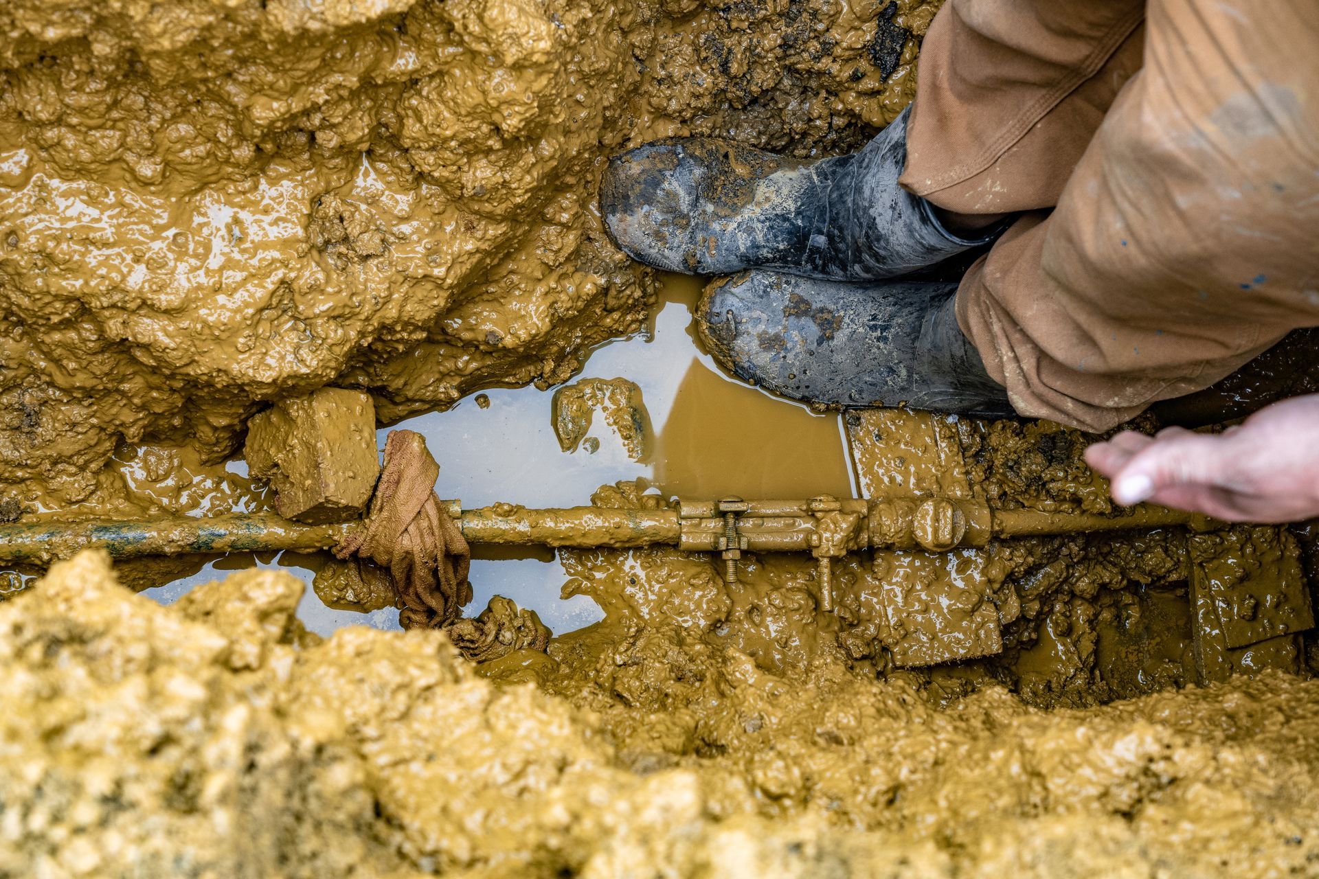 A white pipe is laying in the dirt next to a rock.