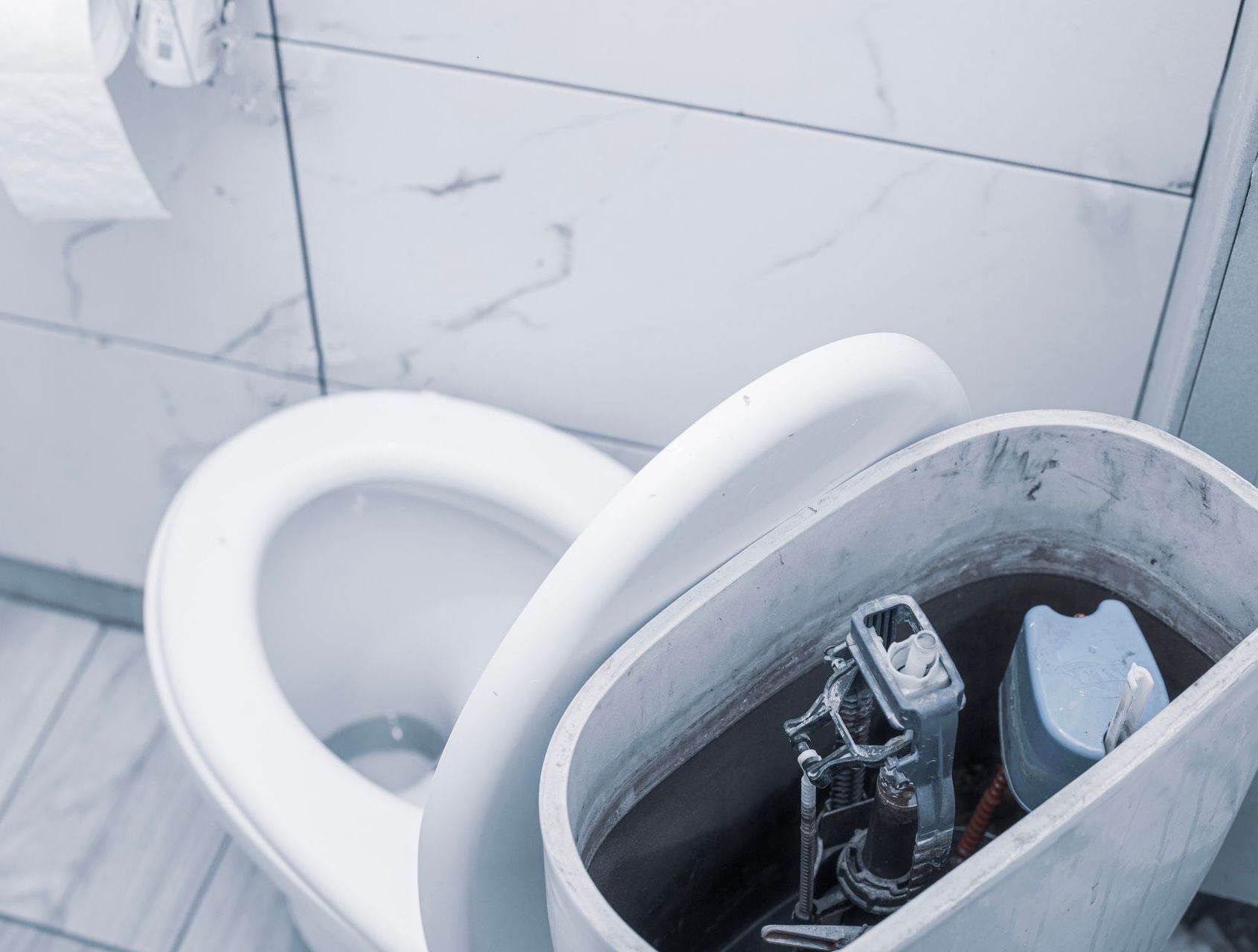 A toilet is being repaired in a bathroom with the lid open.