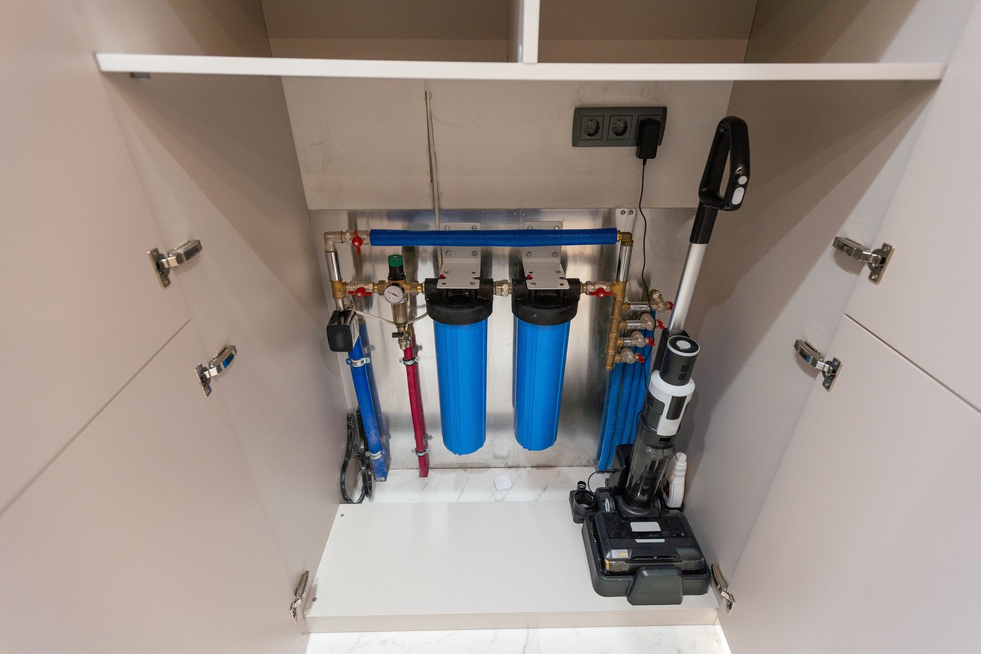 A vacuum cleaner is sitting under a water filter in a cabinet.