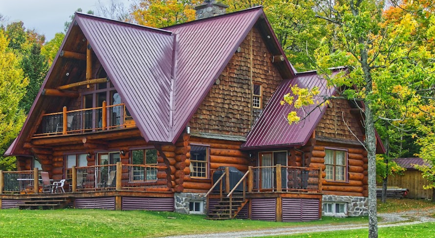 A large log cabin with a red roof is surrounded by trees.