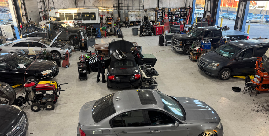 Cars being repaired in a cluttered auto repair shop, various models, tools scattered, workers visible. | St. Louis Auto & Truck Repair
